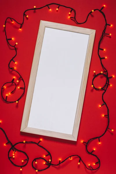 Top view of empty frame and christmas lights isolated on red — Stock Photo