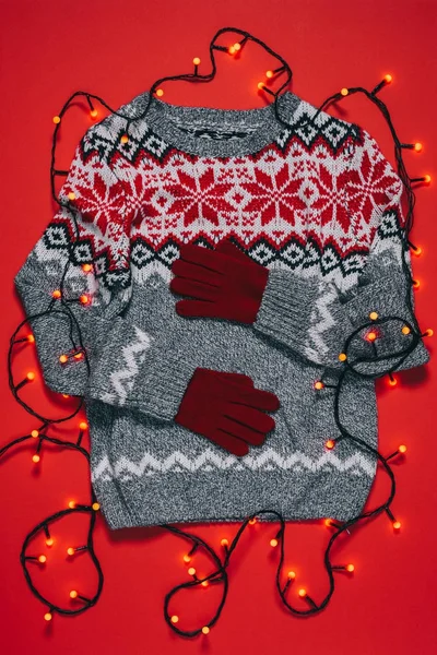 Top view of winter sweater, mittens and christmas lights isolated on red — Stock Photo