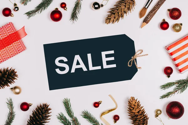 Pose plate avec étiquette de prix arrangé avec lettrage de vente, cônes de pin, cadeaux enveloppés et jouets de Noël isolés sur blanc — Photo de stock