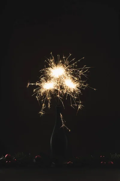 Close up view of burning sparklers in bottle and christmas balls isolated on black — Stock Photo