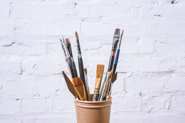 Pinceles en vasos de papel sobre pared blanca — Stock Photo