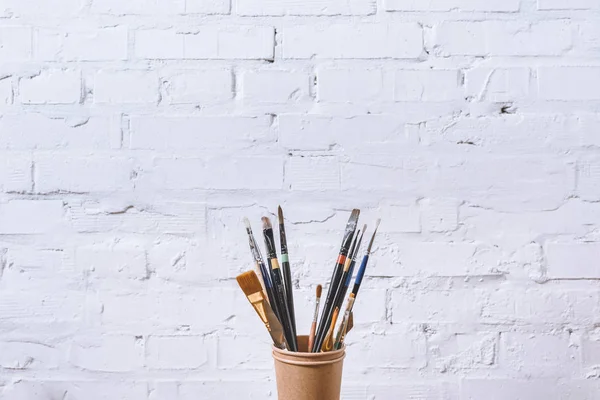 Paint brushes in paper cups on white wall — Stock Photo