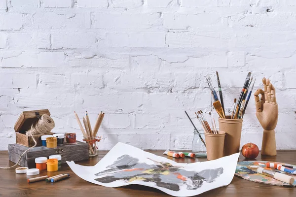Skizze und Tassen mit Pinseln auf Holztisch in Werkstatt — Stockfoto