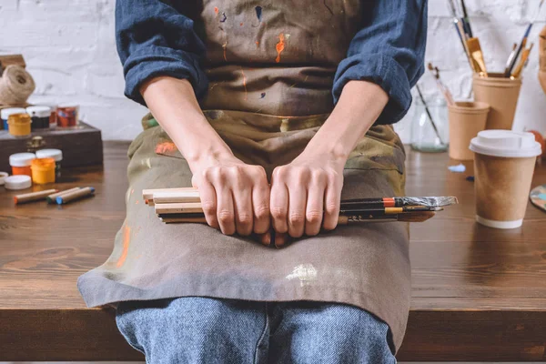 Cropped image of female artist sitting on table and holding brushes — Stock Photo