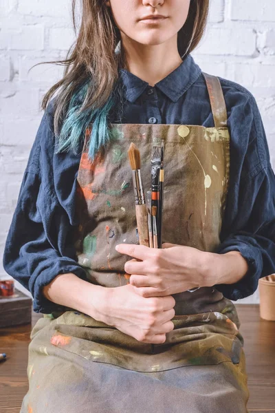 Immagine ritagliata di artista femminile seduta sul tavolo e con pennelli in mano — Foto stock