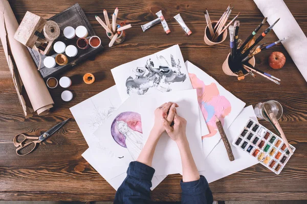 Partial top view of female hands and sketches with paints at artist workplace — Stock Photo