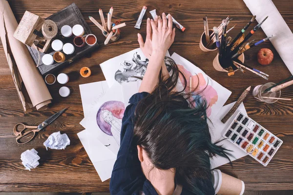 Vue de dessus de l'artiste féminine dormant sur des croquis et des peintures sur le lieu de travail — Photo de stock