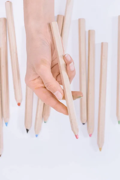 Tiro recortado de la persona sosteniendo crayón rosa con crayones de colores en blanco - foto de stock