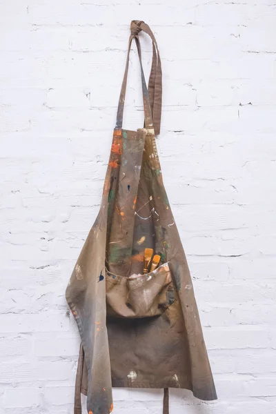 Brown artist apron with paint brushes hanging on brick wall — Stock Photo