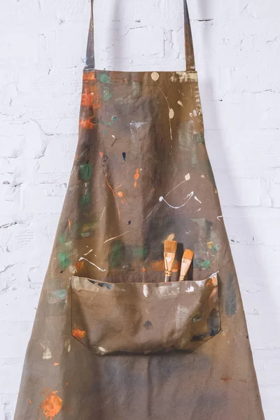 Художній фартух з пензлями для фарби, що висять на цегляній стіні — стокове фото