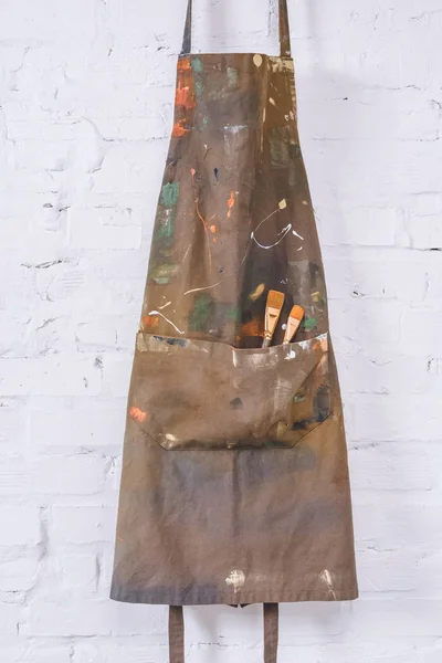 Brown apron with paint brushes hanging on brick wall — Stock Photo