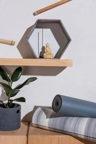 Small statue of buddha in frame with incense stick on wooden shelf, yoga mats near plant — Stock Photo