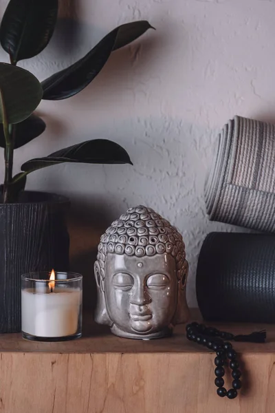Scultura di testa di buddha, candela accesa e stuoie yoga su scaffale di legno — Foto stock