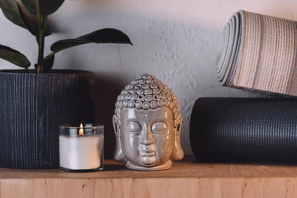 Scultura di testa di buddha, candela accesa e stuoie yoga su scaffale di legno — Foto stock