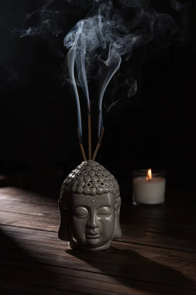 Escultura de la cabeza de buda con varillas de incienso ardiendo y vela en la mesa - foto de stock