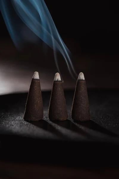 Trois bâtonnets d'encens brûlants avec fumée bleue sur noir — Photo de stock