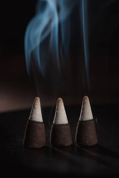 Three burning incense sticks with smoke on dark surface — Stock Photo