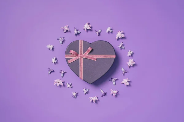 Vue du dessus de boîte cadeau en forme de coeur avec des fleurs autour isolé sur violet — Photo de stock