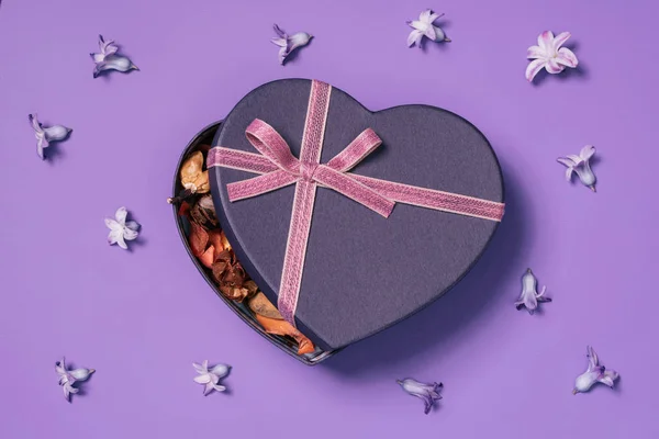 Top view of heart shaped gift box with flowers around isolated on purple — Stock Photo