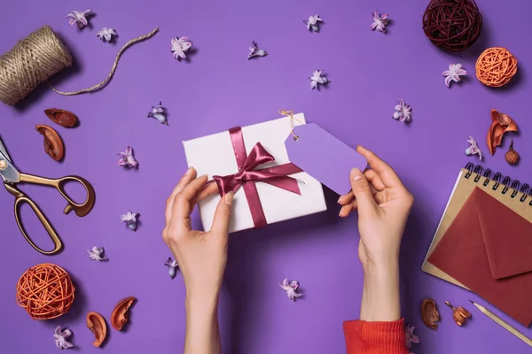 Partial view of woman holding present with card isolated on purple — Stock Photo