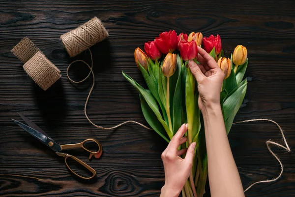 Visão parcial das mãos femininas, corda, tesoura e buquê de flores na superfície de madeira — Fotografia de Stock