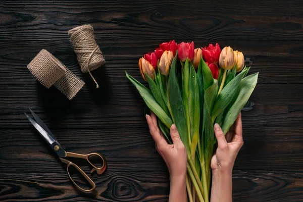 Vista parziale di mani femminili, corda, forbici e mazzo di fiori su superficie di legno — Foto stock