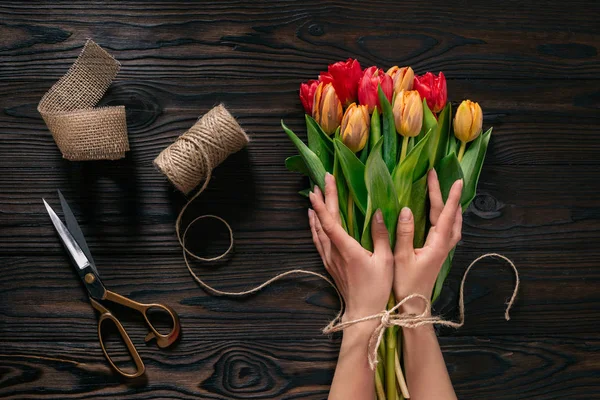 Partial view of female hands, rope, scissors and bouquet of flowers on wooden surface — Stock Photo