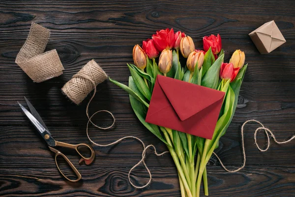 Pose plate avec bouquet de tulipes, enveloppe et fournitures de décoration sur plateau en bois — Photo de stock