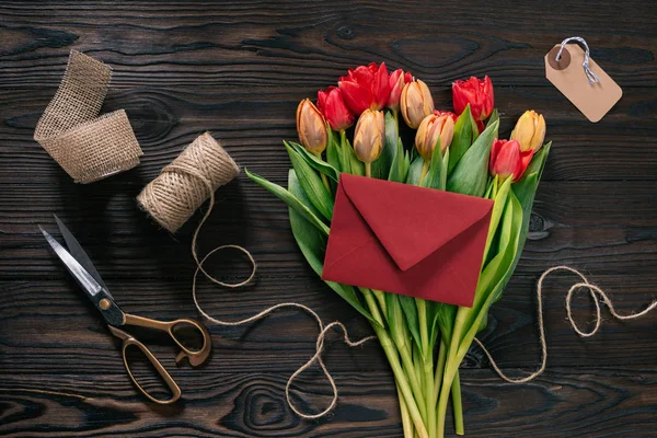 Flat lay com buquê de tulipas, envelope e suprimentos de decoração em mesa de madeira — Fotografia de Stock