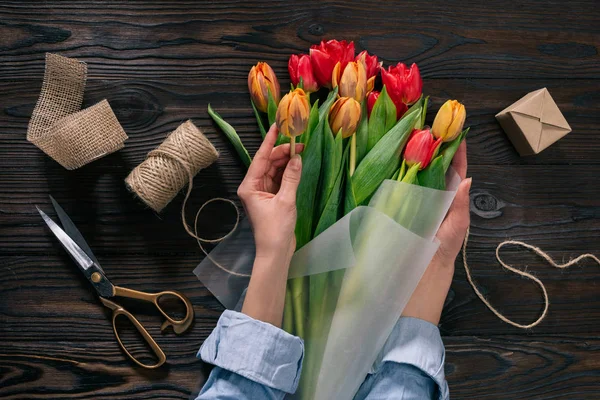 Vue partielle de la femme enveloppant le bouquet de tulipes dans du papier d'emballage sur une table en bois — Photo de stock