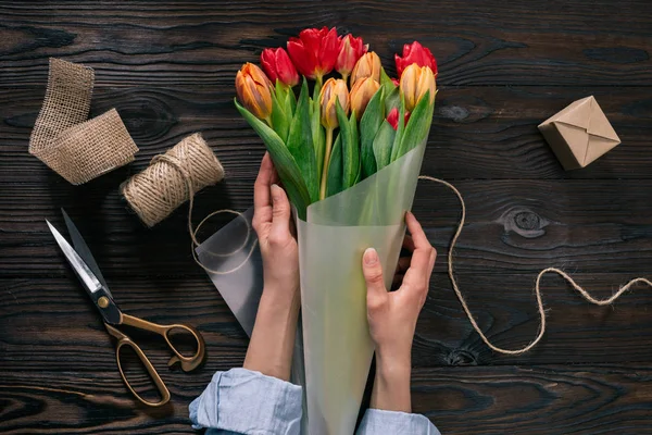 Частичный вид женщины, обертывающей букет тюльпанов в оберточную бумагу на деревянном столе — стоковое фото