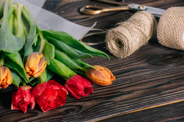 Vista da vicino di bouquet di tulipani, nastro, forbici e corda su un tavolo di legno — Foto stock