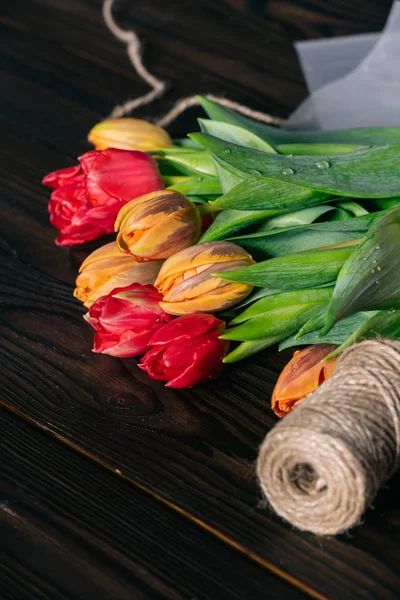 Close up view of bouquet of tulips and rope on wooden tabletop — Stock Photo