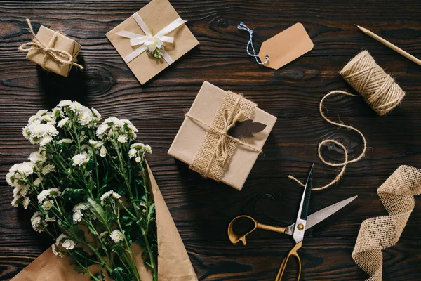 Pose plate avec cadeaux enveloppés, bouquet de fleurs, corde et ciseaux sur la surface en bois — Photo de stock