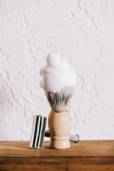 Vue rapprochée de brosse à raser avec mousse et lame contre mur blanc — Photo de stock