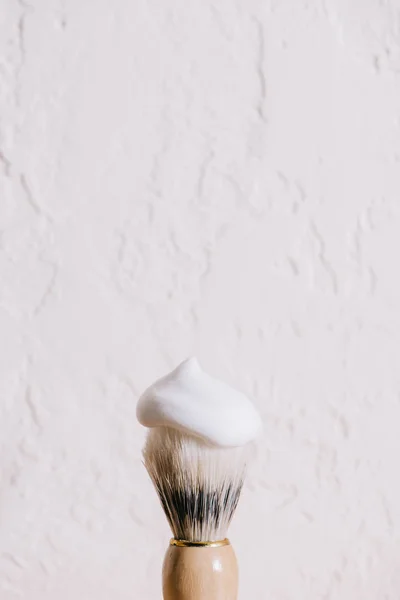 Vista de cerca del cepillo de afeitar con espuma contra la pared blanca - foto de stock
