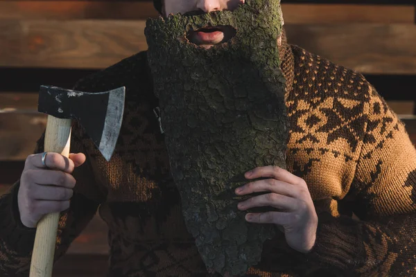 Cropped shot of man with beard made of wood bark and axe in hand outdoors — Stock Photo