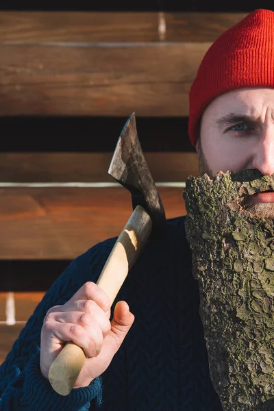 Tiro recortado de hombre con barba hecha de corteza de madera y hacha en la mano al aire libre - foto de stock