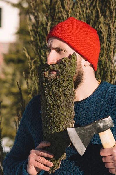 Man with beard made of wood bark and axe in hand looking away outdoors — Stock Photo