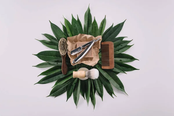 Top view of arranged barber tools for shaving on green leaves isolated on grey — Stock Photo