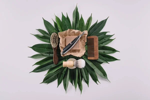 Top view of arranged barber tools for shaving on green leaves isolated on grey — Stock Photo