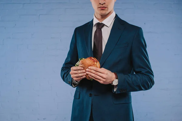 Cropped shot of young businessman in suit holding burger — Stock Photo