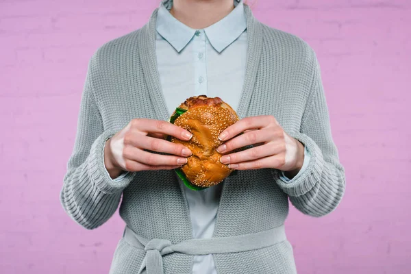 Cropped shot of woman in sweater and shirt holding burger — Stock Photo