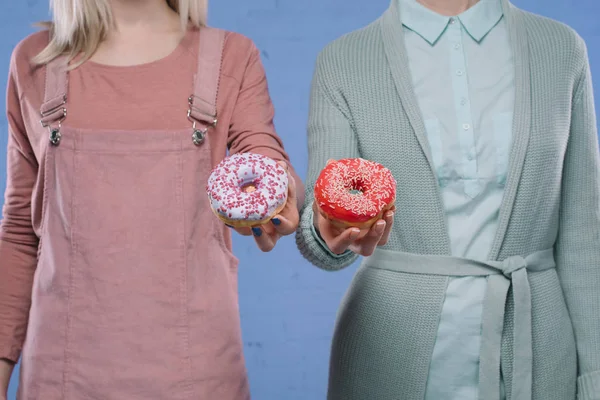 Tiro recortado de mujeres elegantes que sostienen rosquillas vidriadas - foto de stock