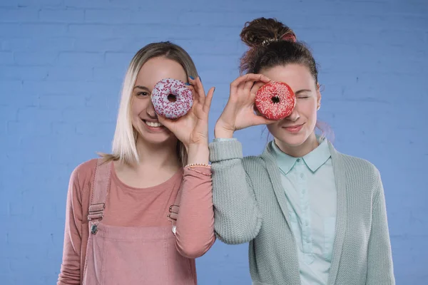 Smiling young women covering eyes with glazed doughnuts — Stock Photo