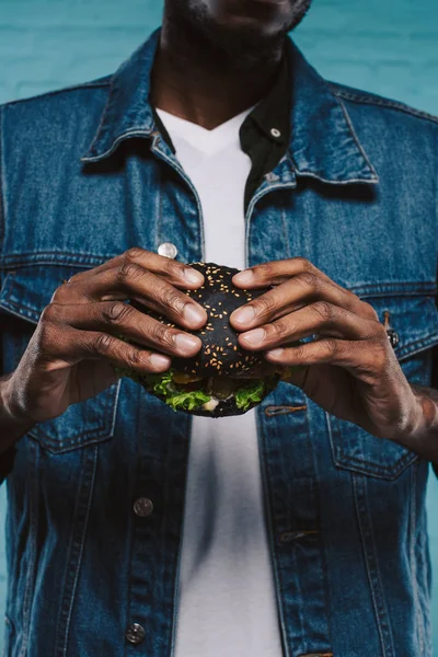 Cropped shot of african american man holding black burger — Stock Photo