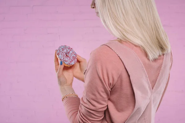 Colpo ritagliato di giovane donna guardando ciambella davanti al muro di mattoni rosa — Foto stock