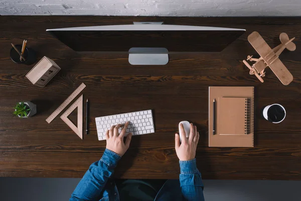 Vista superior parcial de la persona que escribe en el teclado y el uso de computadora de escritorio en el lugar de trabajo - foto de stock