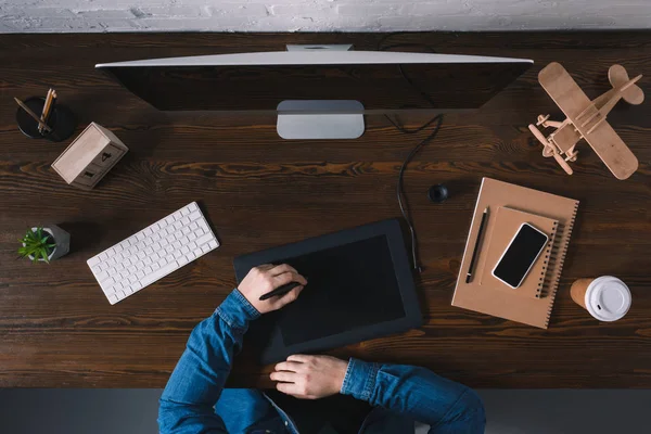 Vista superior parcial de la persona que usa la tableta gráfica mientras está sentado en el lugar de trabajo - foto de stock