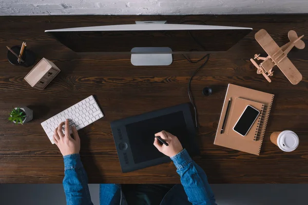 Vista superior de la persona que utiliza la tableta gráfica y escribir en el teclado en el lugar de trabajo - foto de stock